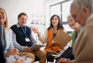 Excited elderly people attending a group therapy session at nursing house, positive senior man and woman sitting in circle, having conversation with psychologist - HPIF00378
