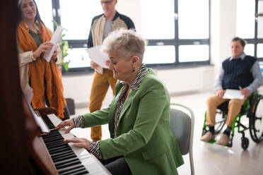 A senior woman playing at piano in choir rehearsal. - HPIF00383