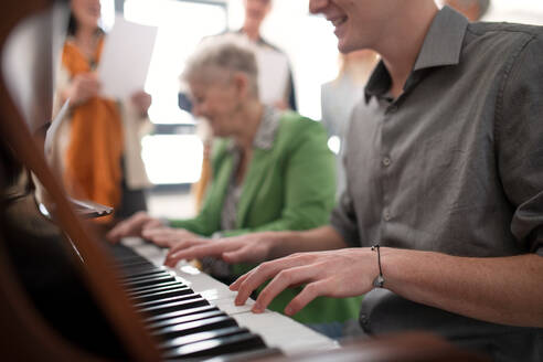 Eine ältere Frau mit einer jungen Lehrerin, die bei einer Chorprobe am Klavier spielt. - HPIF00386