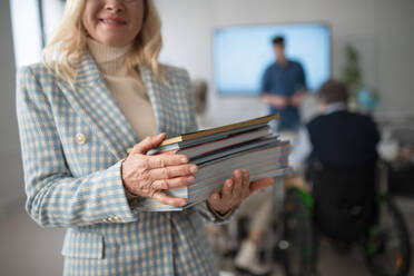 Glückliche ältere Studentin posiert mit einem Buch im Klassenzimmer. - HPIF00422