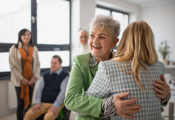 Glückliche ältere Studentinnen, die sich in einem Klassenzimmer treffen und umarmen. - HPIF00429