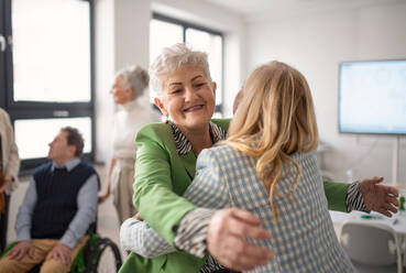 Glückliche ältere Studentinnen, die sich in einem Klassenzimmer treffen und umarmen. - HPIF00430
