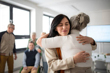 Happy senior women students meeting and hugging in a classroom. - HPIF00432