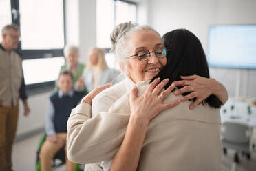 Glückliche ältere Studentinnen, die sich in einem Klassenzimmer treffen und umarmen. - HPIF00433