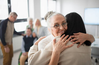 Glückliche ältere Studentinnen, die sich in einem Klassenzimmer treffen und umarmen. - HPIF00434