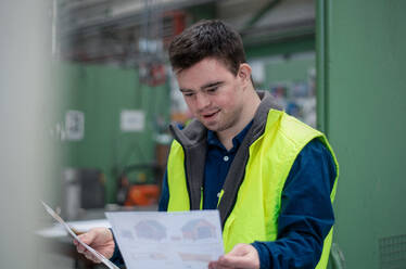 A young man with Down syndrome looking at blueprints when working in industrial factory, social integration concept. - HPIF00512