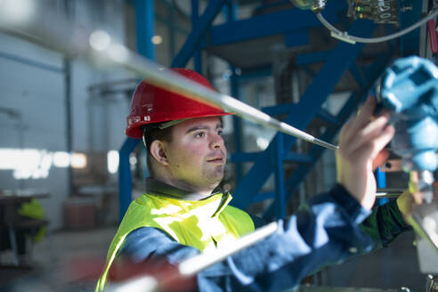 A young man with Down syndrome working in industrial factory, social integration concept. - HPIF00529
