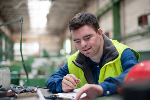 A young man with Down syndrome working in industrial factory, social integration concept. - HPIF00542