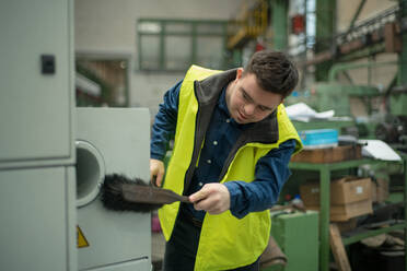 A young man with Down syndrome working in industrial factory,cleaning workspace, social integration concept. - HPIF00549