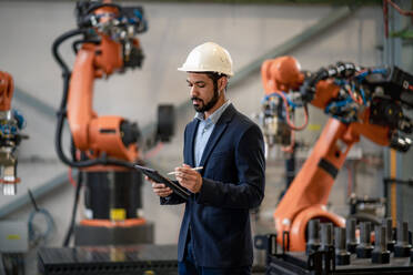 An automation engineer uses tablet for programming robotic arm in factory. - HPIF00584