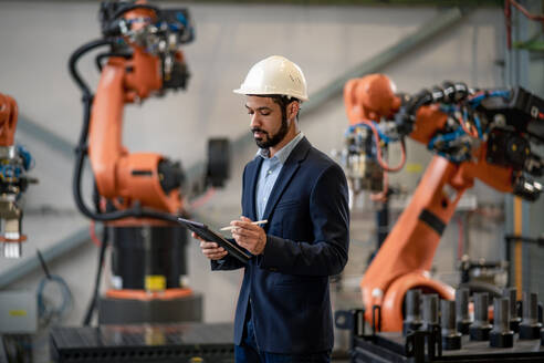 Ein Automatisierungsingenieur verwendet ein Tablet zur Programmierung eines Roboterarms in einer Fabrik. - HPIF00584