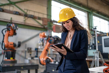 Eine Automatisierungsingenieurin mit Tablet zur Programmierung eines Roboterarms in einer Fabrik. - HPIF00590