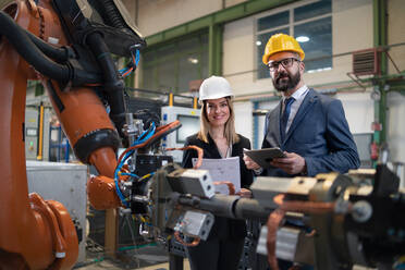 Ein Chefingenieur und Projektleiter in einer modernen Industriefabrik mit Roboterarmen, die über die Optimierung der Produktion sprechen und diese planen. - HPIF00594