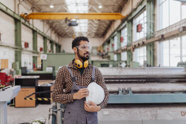 Ein Schwerindustriearbeiter mit Sicherheitskopfhörern und Schutzhelm in einer Industrieanlage - HPIF00632