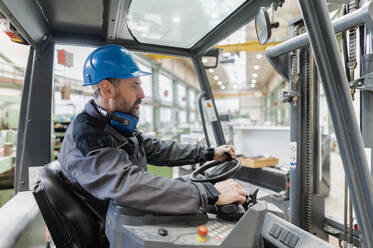 A happy mature man fork lift truck driver lifting pallet in storage warehouse . - HPIF00649