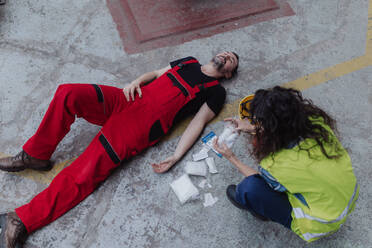 Eine Frau hilft ihrem Kollegen nach einem Unfall in einer Fabrik. Erste-Hilfe-Unterstützung am Arbeitsplatz. - HPIF00675