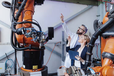 Robotics engineers with a tablet dicussing and desinging modern robotic arm in factory. - HPIF00689