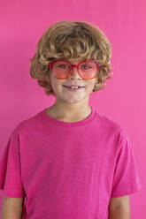 Smiling boy wearing colored sunglasses against pink background - MEGF00162