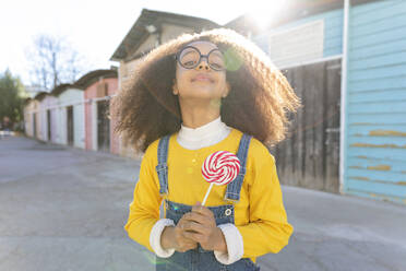 Mädchen mit Brille hält Lutscher an einem sonnigen Tag - MEGF00201