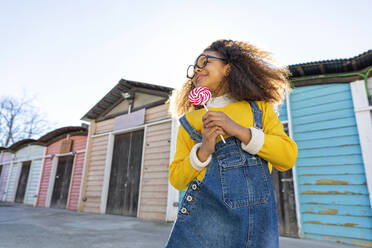 Girl with lollipop in front of beach huts - MEGF00203