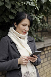 Woman wearing scarf using smart phone by plants - ONAF00278