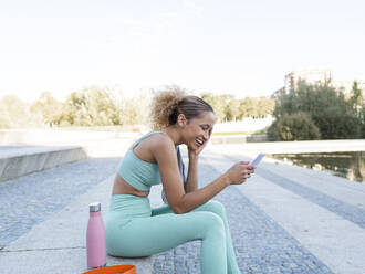 Glückliche Sportlerin mit Smartphone auf der Treppe - AMRF00180