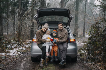 Glückliche Familie mit Kaffeetassen im Kofferraum eines Autos - NDEF00240