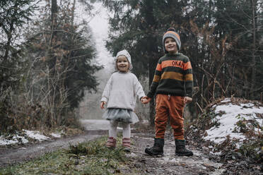 Glückliche Geschwister, die sich an den Händen halten, stehen im Wald - NDEF00243