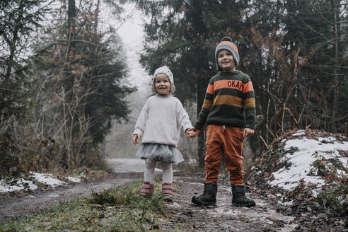 Happy siblings holding hands standing in forest - NDEF00243