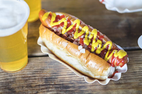 Senf und Ketchup auf Hot Dog mit einem Glas Bier am Tisch - IFRF01895