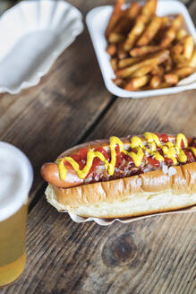 Senf und Ketchup auf Hot Dog mit Pommes frites am Tisch - IFRF01896
