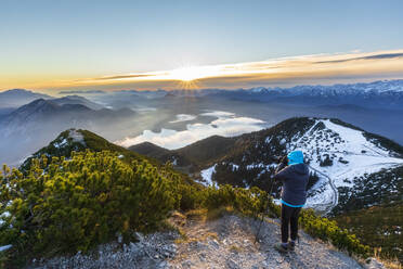 Deutschland, Bayern, Frau fotografiert die umliegende Landschaft vom Gipfel des Herzogstands bei Sonnenaufgang - FOF13187