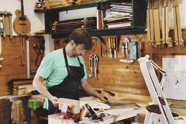 Gitarrenbauer bei der Arbeit an der Schablone einer Gitarre in der Werkstatt - JSMF02546