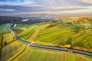 Germany, Baden-Wurttemberg, Drone view of country road stretching between autumn fields at dawn - STSF03695