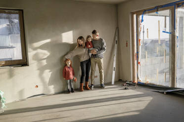 Geschwister mit Eltern, die vor einer Mauer in einem unvollständigen Haus stehen - VIVF00230
