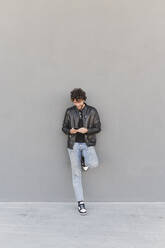 Mann mit Smartphone lehnt an grauer Wand - FMOF01578