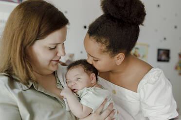 Happy mother with daughter kissing baby girl at home - VIVF00262