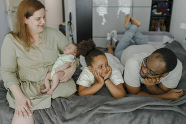 Happy mother carrying baby girl with father and daughter lying on bed at home - VIVF00271