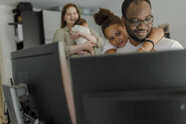 Lächelnder Mann arbeitet am Computer mit seiner Tochter, die ihn von hinten umarmt - VIVF00290