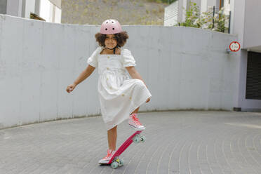 Lächelndes Mädchen mit Helm beim Skateboarden auf dem Fußweg - VIVF00294