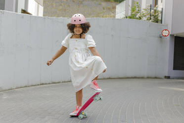 Smiling girl wearing helmet skateboarding on footpath - VIVF00294