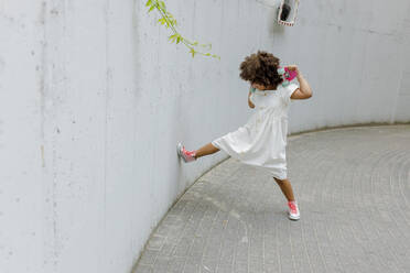 Mädchen steht mit Skateboard und tritt gegen die Wand am Fußweg - VIVF00297