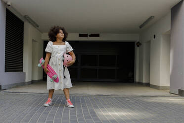 Girl standing with skateboard and helmet in front of garage entrance - VIVF00311