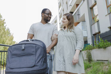 Smiling man and woman walking with stroller in front of building - VIVF00313