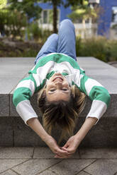 Happy young woman lying on concrete bench - WPEF06698