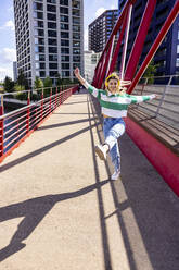 Happy young woman listening to music through headphones enjoying on walkway - WPEF06703