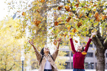 Glückliche junge Frauen, die Herbstblätter werfen und sich im Park vergnügen - WPEF06726