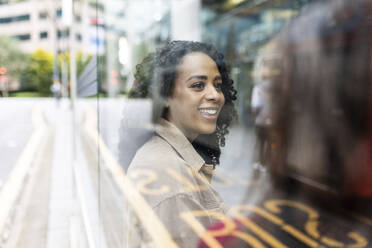 Glückliche Frau, die mit einem Freund an der Bushaltestelle sitzt, gesehen durch Glas - WPEF06749