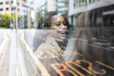 Happy woman talking to friend at bus stop seen through glass - WPEF06750