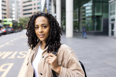 Smiling woman with curly hair on footpath at bus stop - WPEF06759